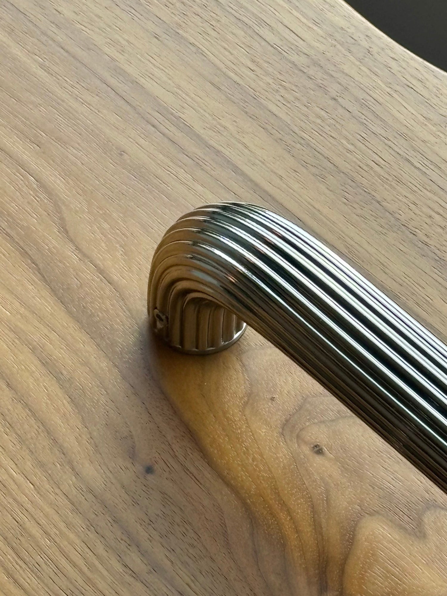 A close-up of a polish nickel grab bar with a ribbed, fluted design, mounted on a warm wood-grain surface.