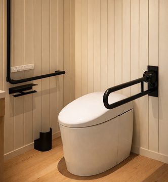 Sleek wall-hung smart toilet with sculptural matte black safety bar in a Japandi-inspired wood-paneled bathroom — where high design meets everyday ease