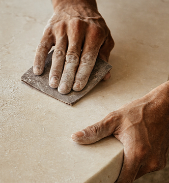 Artisan hands finishing a natural limestone countertop — custom stonework and handcrafted material selection for bespoke bathroom remodels